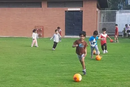 A young player runs with the ball across a large grassy field. We provide ample space for kids to practice their skills and enjoy the freedom of the game.