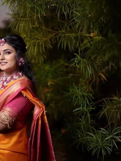 A stunning bridal portrait taken at dusk. The bride, dressed in a traditional orange and pink saree for her Haldi ceremony, is beautifully lit against a dark green background.