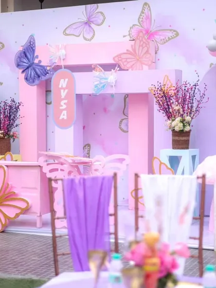 A view of the kids' seating area at the butterfly party, with chairs draped in purple fabric and a stunning, multi-layered backdrop.