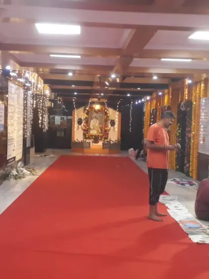 The initial setup for a community event in Bandra East, with a red carpet runner and traditional marigold flower decorations lining the hall.