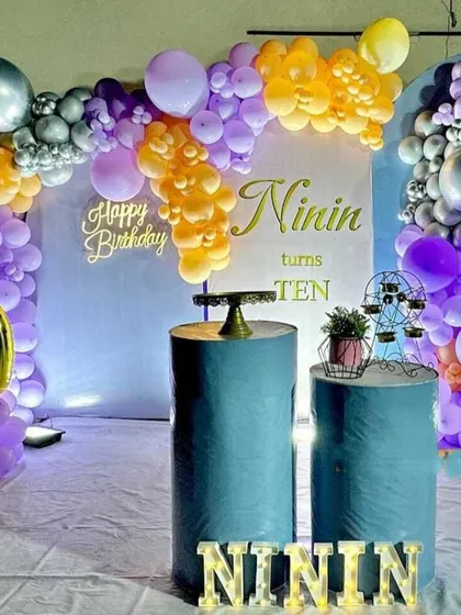 A tenth birthday party with a purple, orange, and silver balloon arrangement. The decor includes a large foil number '10' and marquee letters.