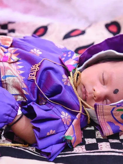 A peaceful photo of the newborn baby sleeping soundly during her naming ceremony, dressed in a beautiful traditional outfit.
