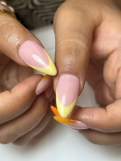 A close-up of the sunkissed neon French tips, showing the smooth blend of yellow and orange on a sharp stiletto nail.