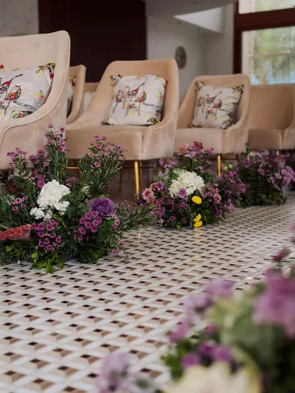 A closer look at the pastel suede seating and the aisle lined with pockets of purple and white flowers, creating a soft and romantic ambiance.