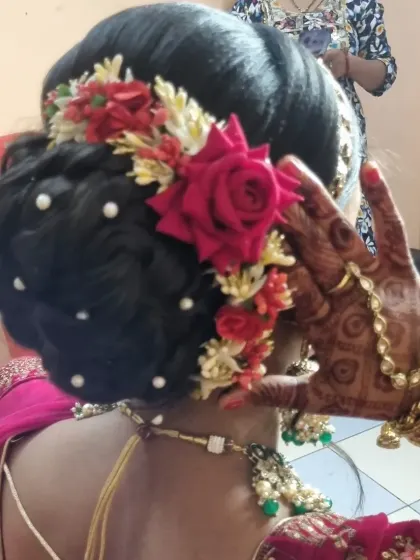 This bridal look features a beautiful red and green color combination. The hairstyle is a classic bun decorated with red roses and pearls, complementing her stunning lehenga.