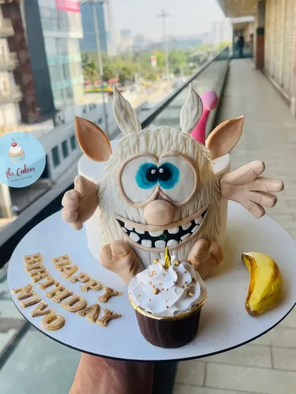 A playful and highly detailed 3D cake of Booba, the curious cartoon creature. This sculpted cake comes with a matching cupcake and a fondant banana, capturing the character's fun personality perfectly.