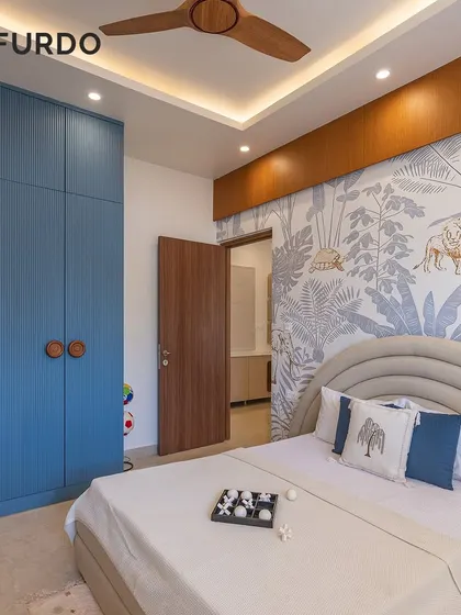 A playful yet stylish bedroom with a jungle-themed wallpaper accent. The fluted blue wardrobe with custom wooden handles adds a pop of color and texture to the room.