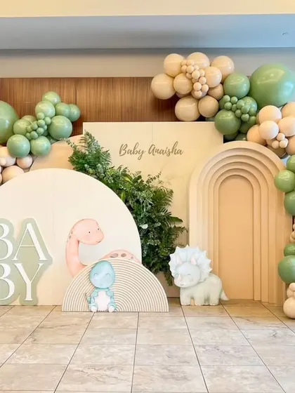 A dino-mite baby shower setup. This design uses a soft, neutral color palette with sage green and beige balloons, paired with cute dinosaur cutouts for a modern and stylish take on the theme.
