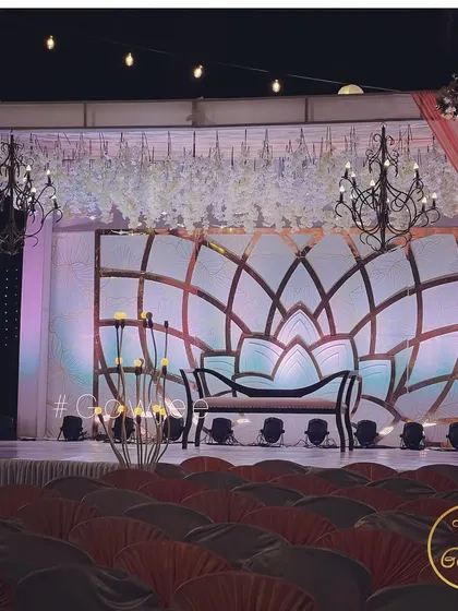An elegant reception stage with a large lotus-motif backdrop, black chandeliers, and soft pink draping.