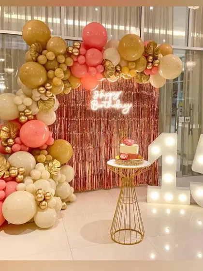 A beautiful rose gold and peach balloon arch against a foil curtain backdrop, perfect for a 15th birthday.