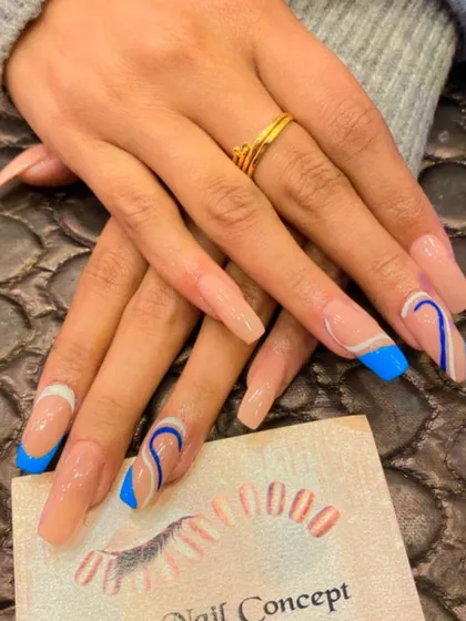 A modern and artistic design on long, square nails. The nude base is decorated with a mix of blue French tips and abstract blue and white swirls.