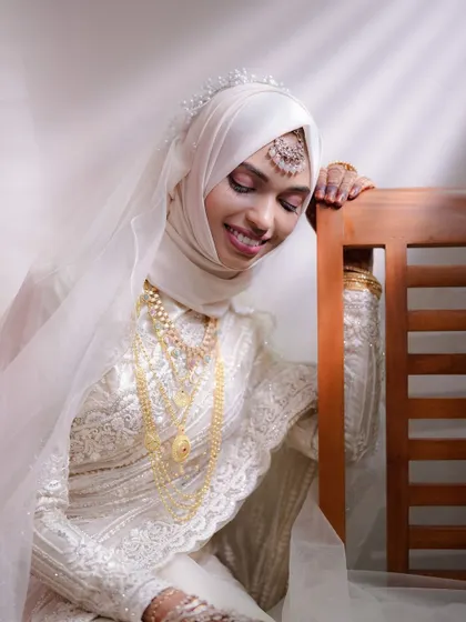 The bride, dressed in elegant white lace and gold jewelry, smiles softly in this beautiful, light-filled portrait.