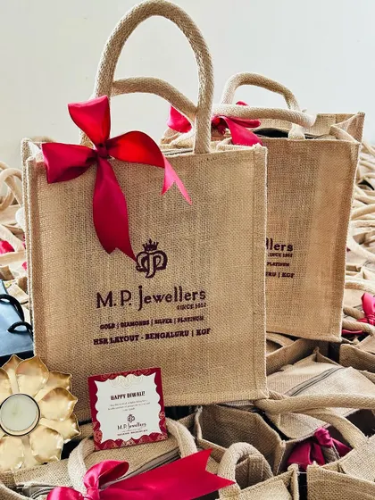 A festive return gift set, perfect for Diwali. It includes a custom jute bag, a greeting card, and a decorative diya.