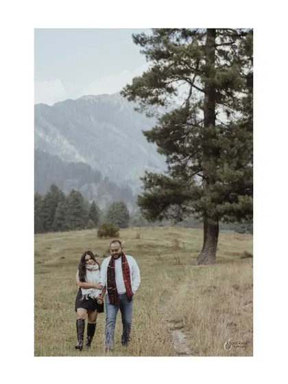 A candid walking shot of Ayushi and Vaibhav during their Kashmir pre-wedding shoot, set against a backdrop of pine trees and mountains.