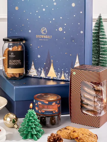 A detailed look at the contents of a Christmas gift box. You can see the almond biscotti, assorted cookies, a festive candle, and other treats, all carefully arranged for a beautiful presentation.