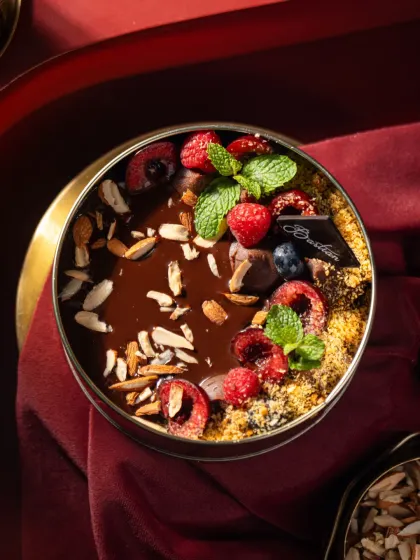 A top-down view of a berry and chocolate cheesecake from Bastian. The rich red background and fresh mint garnish make the colours pop in this luxurious dessert shot.