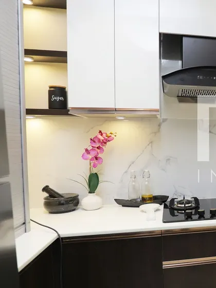A close-up of a modern kitchen with a white marble backsplash and dark wood cabinets. The sleek black hob and decorative orchid add to the elegant and clean aesthetic.