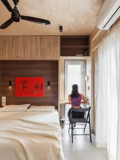 This bedroom in a compact apartment is designed for flexibility. It features a dedicated study nook by the window for work, ample wardrobe storage, and a Murphy bed that can be folded away to create open space for activities like yoga or workouts.