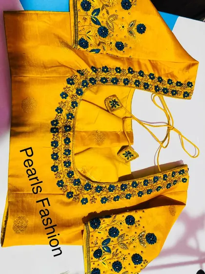 A mustard yellow blouse with blue floral threadwork. The flowers are placed along the neckline and scattered on the sleeves, with matching latkans.