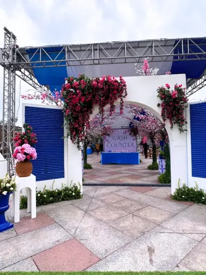 A grand entrance designed to feel like stepping into a Santorini postcard. The white and blue structure is adorned with bougainvillea, creating a fresh and festive welcome for a carnival-themed event.