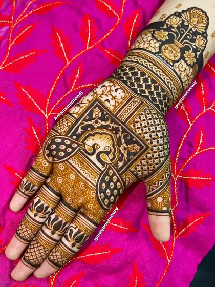 A bold and beautiful back-of-hand design. The central peacock is framed by a square, with a kalash (sacred pot) on the wrist, all set against a dark, filled-in background.