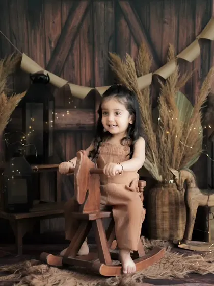 A rustic, cozy studio setup for a pre-mundan shoot. The warm wooden background, pampas grass, and a rocking horse create a charming and playful atmosphere.