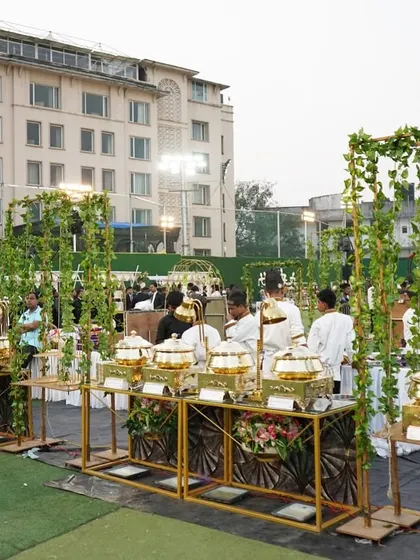 A beautiful outdoor buffet arrangement with golden stands and lush green vine decorations. This setup is perfect for a daytime garden wedding, blending seamlessly with the natural surroundings while providing a touch of elegance.