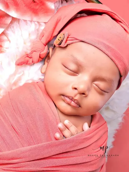 A close-up of a sleeping baby in a peach-colored wrap and hat.