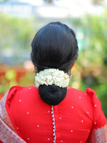 A simple, clean, and traditional bridal bun adorned with a string of fresh jasmine flowers. This look is timeless and complements a classic red saree perfectly.