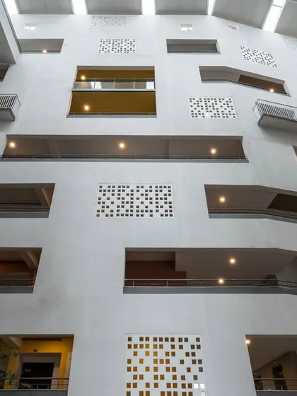 The dynamic interior facade of the atrium, with its varied openings and perforated screens, creates a sense of depth and complexity. This design moves away from the typical flat corridors of residential buildings.