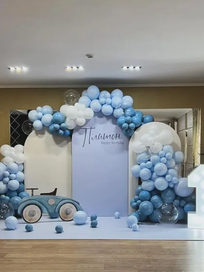 A chic and minimalist first birthday setup in pastel blue, featuring a vintage car prop, a light-up marquee number '1', and balloon clouds.