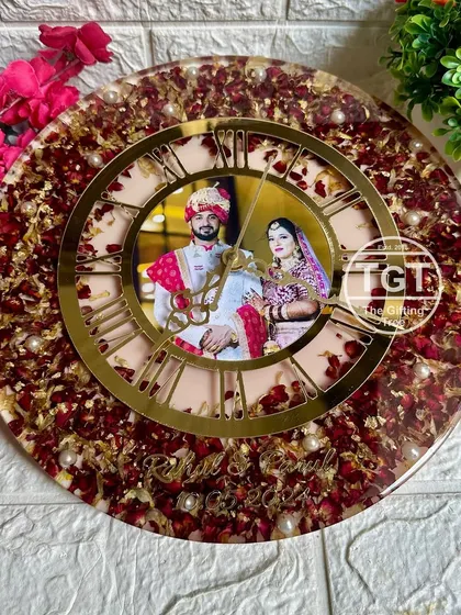 The combination of red rose petals, gold flakes, and pearls creates a dense, textured border around the central clock face, making this a truly opulent wedding keepsake.