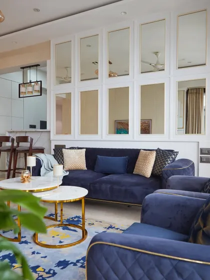 A view of a living room from a Lodha project, highlighting the blue quilted sofas, marble breakfast counter, and a distinctive mirror-paneled wall.