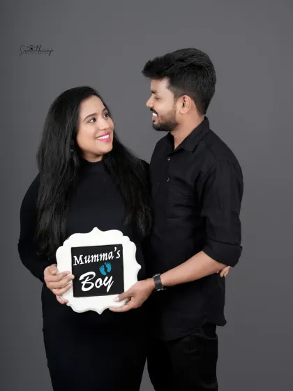 A happy couple portrait announcing "Mumma's Boy." Their matching black outfits and the cute sign create a sweet and personal gender reveal photo.