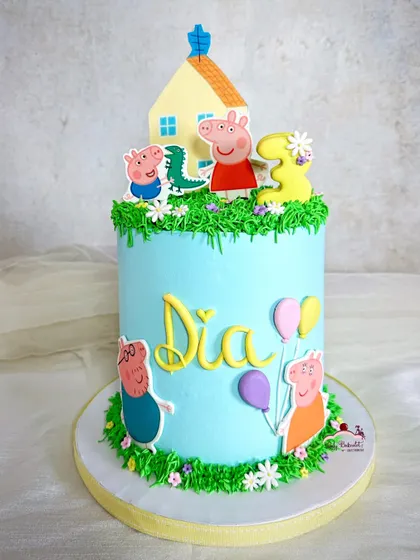 A cheerful Peppa Pig cake with Peppa, George, and their little house on a grassy hill. The buttercream grass and flowers add a fun, playful texture.
