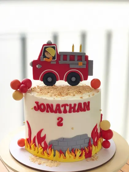 A cute firetruck cake for a second birthday, with a handcrafted truck topper, flames, and a brick wall design.