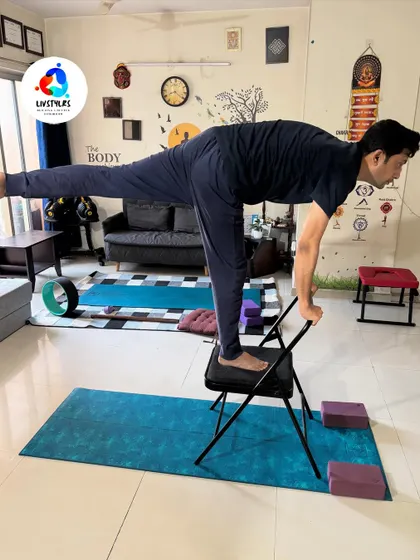A client practices Virabhadrasana III (Warrior III) with the support of a yoga chair. This modification helps to build balance, strength, and focus without the risk of falling.