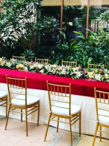 I also provide decor for guest dining areas to ensure a cohesive look. This long table is elegantly styled with a rich red tablecloth, a fresh floral runner, and classic gold Chiavari chairs for a formal dinner.