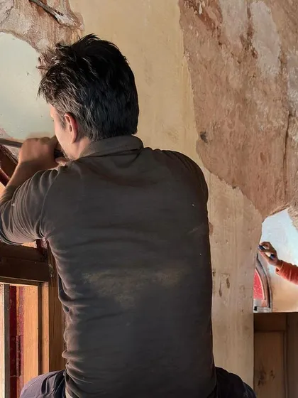Two craftsmen work on restoring the arched windows from inside. The image shows the collaborative effort involved in bringing these beautiful architectural features back to life.