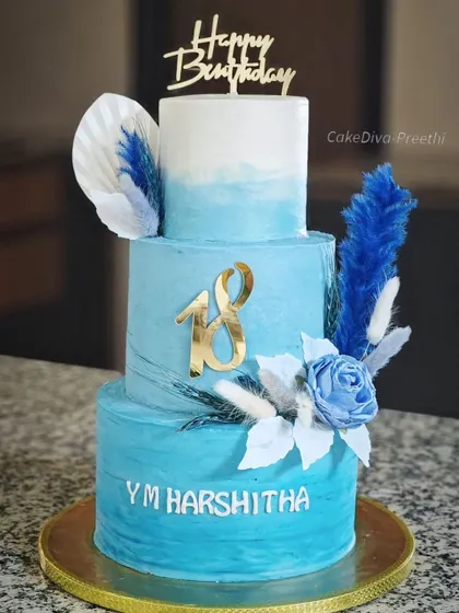 A full view of the stunning three-tiered 18th birthday cake. The ombre blue buttercream, dried floral arrangements, and personalized name create a truly memorable and photo-worthy celebration cake.
