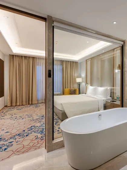 A guest suite featuring an open-concept layout where a freestanding bathtub is visually connected to the bedroom. This design creates a luxurious and spacious feel, enhanced by a large glass partition.