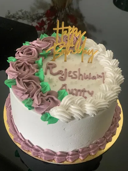 A classic floral birthday cake. The white cake is decorated with a crescent of purple and white buttercream roses.