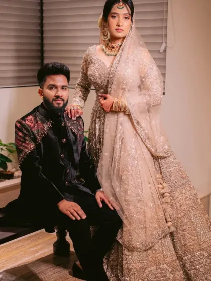A portrait of regal elegance. This couple's engagement attire features a heavily embellished lehenga for her and a bespoke black velvet sherwani with detailed shoulder work for him.