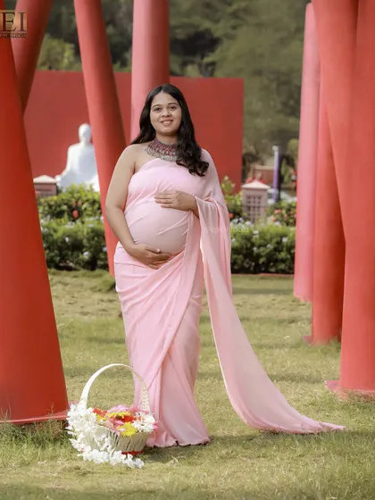 A solo portrait in a flowing pink saree, taken at an outdoor location with striking red architectural pillars.
