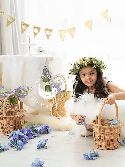 A candid moment during a toddler playtime session. She's exploring the floral props with a sweet, curious expression.