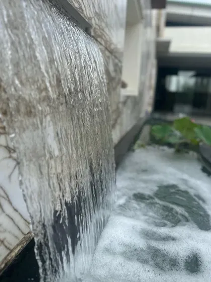 A close-up of a water feature, where water cascades down a textured marble wall into a pond. We use these details to add sensory experiences to our architectural designs.