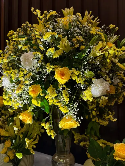 A bright and cheerful floral arrangement dominated by yellow roses and lilies. This is perfect for adding a touch of sunshine to any celebration, be it a wedding or a festive gathering.