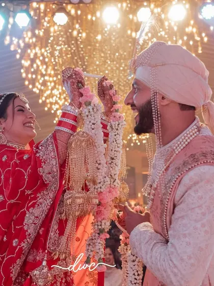 Another angle of a joyous Jaimala, capturing the couple's laughter and the grand, sparkling decor of the wedding venue.
