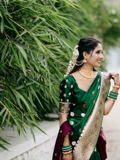 A beautiful candid portrait of the bride in her stunning green Paithani saree. Her joyful, natural smile is captured against a backdrop of vibrant bamboo, highlighting the elegance of the traditional Maharashtrian bridal look.
