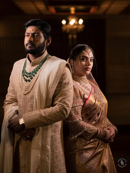A regal portrait of the couple in their wedding attire, standing back-to-back, showcasing their stunning outfits and jewelry.